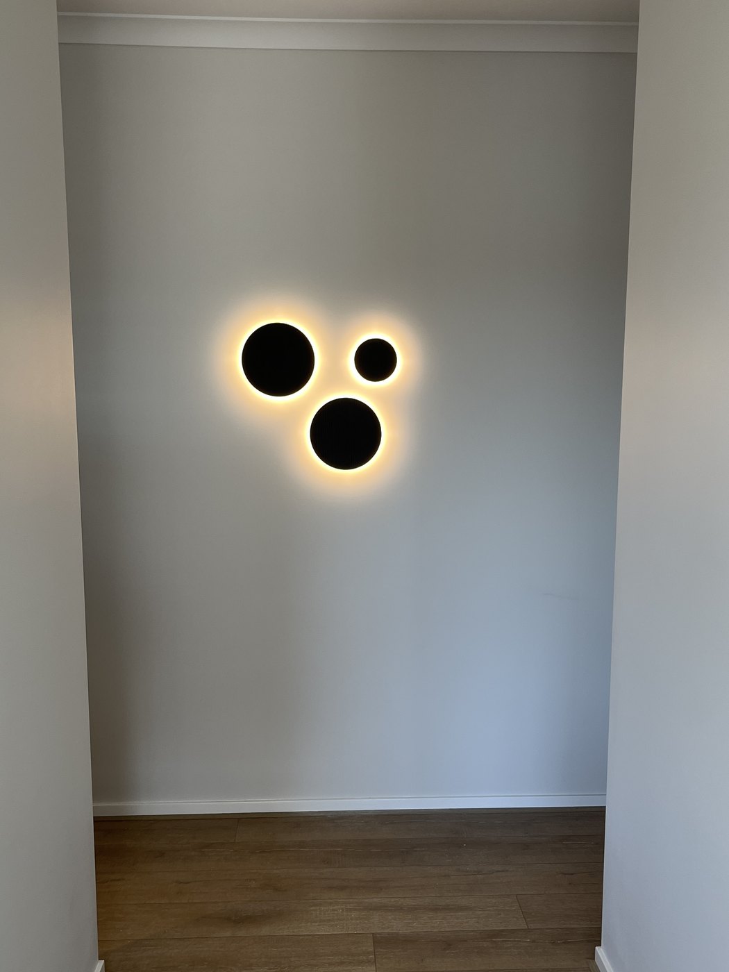 Backlit three-disc black wall light mounted in a white alcove, installed by SALTD Electrical