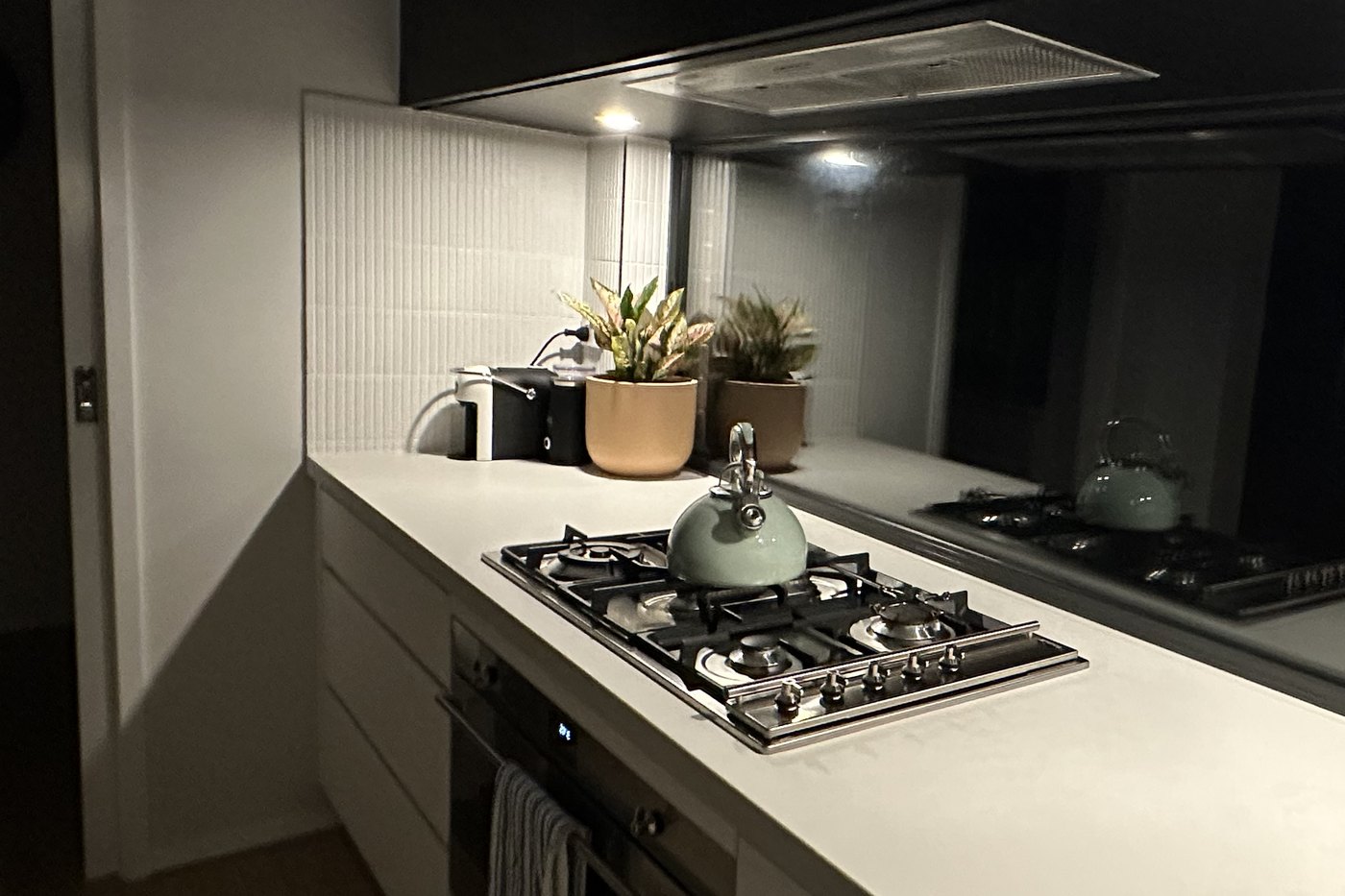 Kitchen at night lit by an under-cabinet strip and a rangehood light reflecting off a mirrored splashback, installed by SALTD Electrical