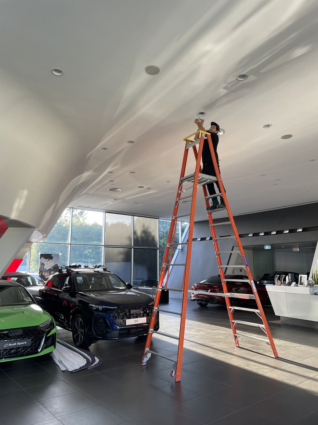 SALTD Electrical replacing a ceiling downlight from a ladder in a car dealership showroom