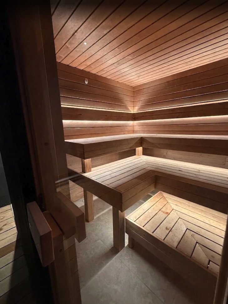 Home sauna lined in timber, lit by LED strips concealed under each bench tier and along the upper wall, installed by SALTD Electrical
